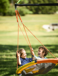 Two smiling children excitedly playing on a Sky Adventure Swing outdoors in a park.