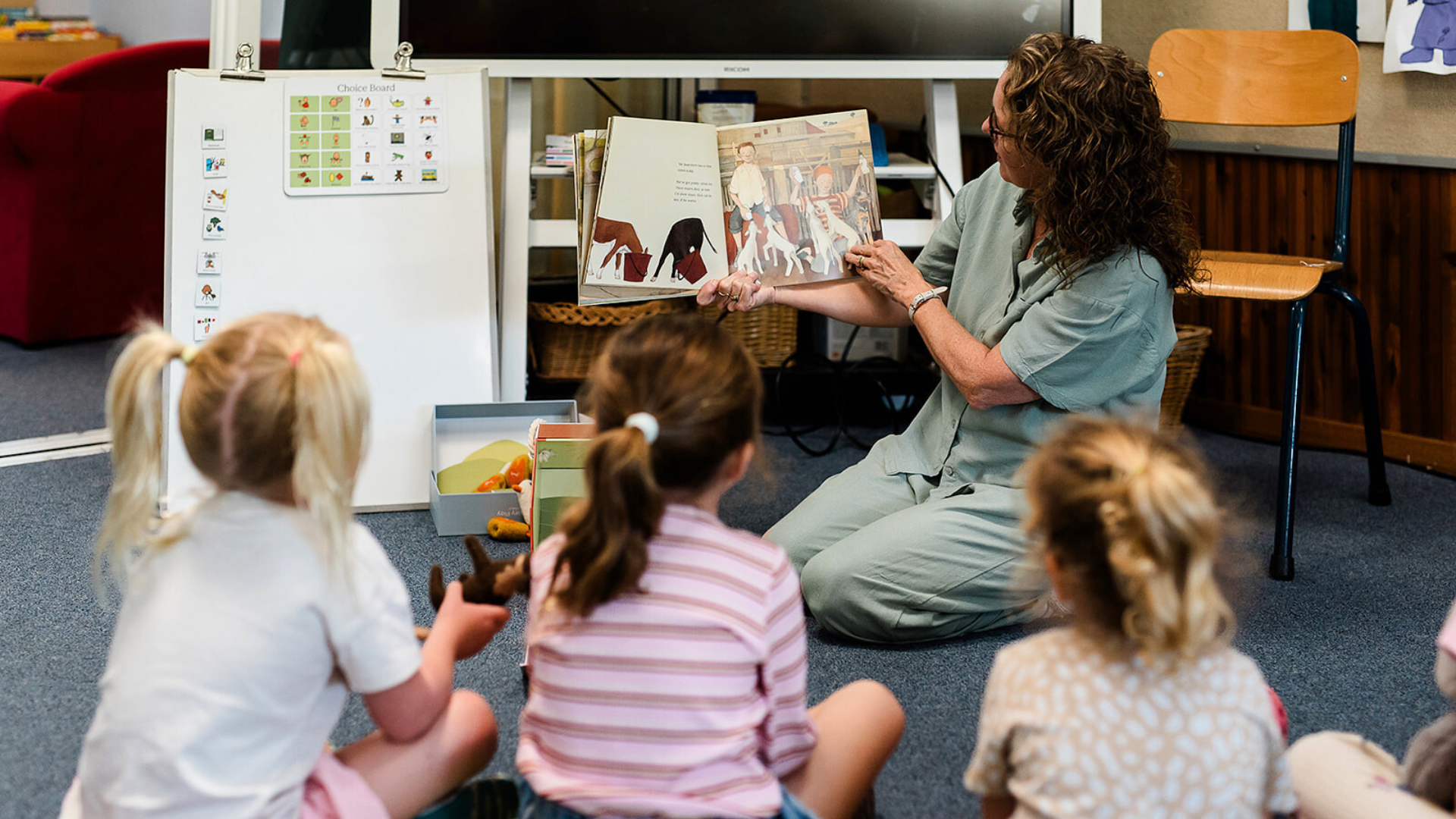 Teacher reading a book to children in a classroom setting.