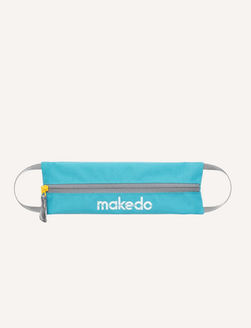 An open blue makedo Tool-Case reveals yellow tools and blue connectors inside. Extra connectors and a tool lie on the beige textured surface nearby, with a partially visible box in the background.