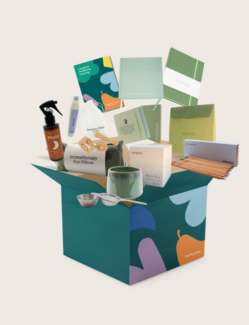 The Therapy At Home Caregiver Wellbeing Training Program includes a ceramic mug, bath salts, aromatherapy eye pillow, tea, notepads, colored pencils, and booklets—perfect for supporting caregiver wellbeing and emotional regulation.