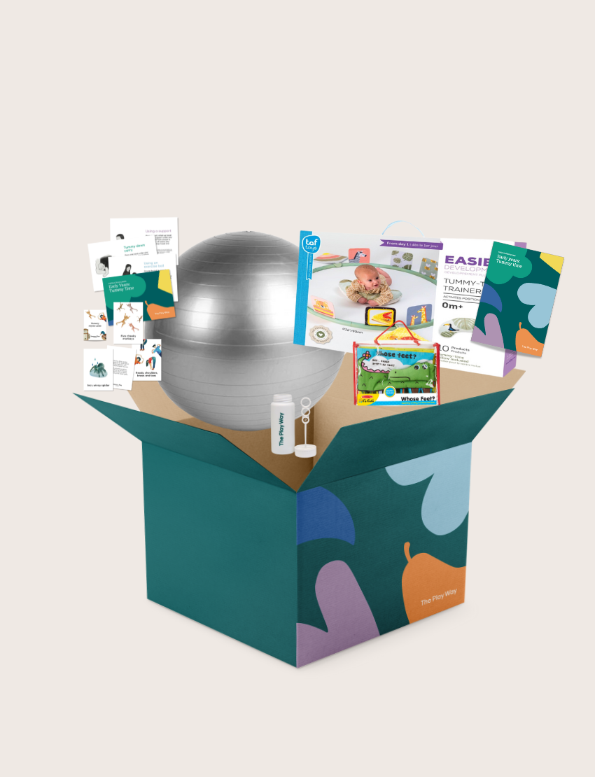 The Tummy Time Program by Therapy At Home comes in an open teal box with abstract shapes and includes a silver exercise ball, bubble wand, baby food pouch, cards, leaflets, and packaging for baby development and parent guides.