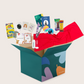 A large teal box with colorful shapes, labeled "Calm Down Kit" by The Play Way, contains educational toys like books, a puzzle, a coloring set, and crafting materials. A red cloth and a tag are also visible.