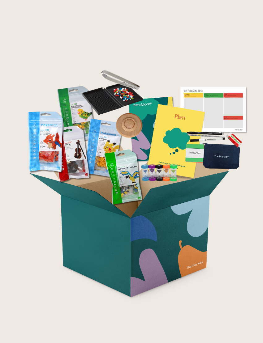 The Nanoblock Program by Therapy At Home includes an open teal box with activity booklets, craft materials, paint pots, modeling clay, stickers, a spinning top, utensils, and a magnetic chart to build executive functioning skills.