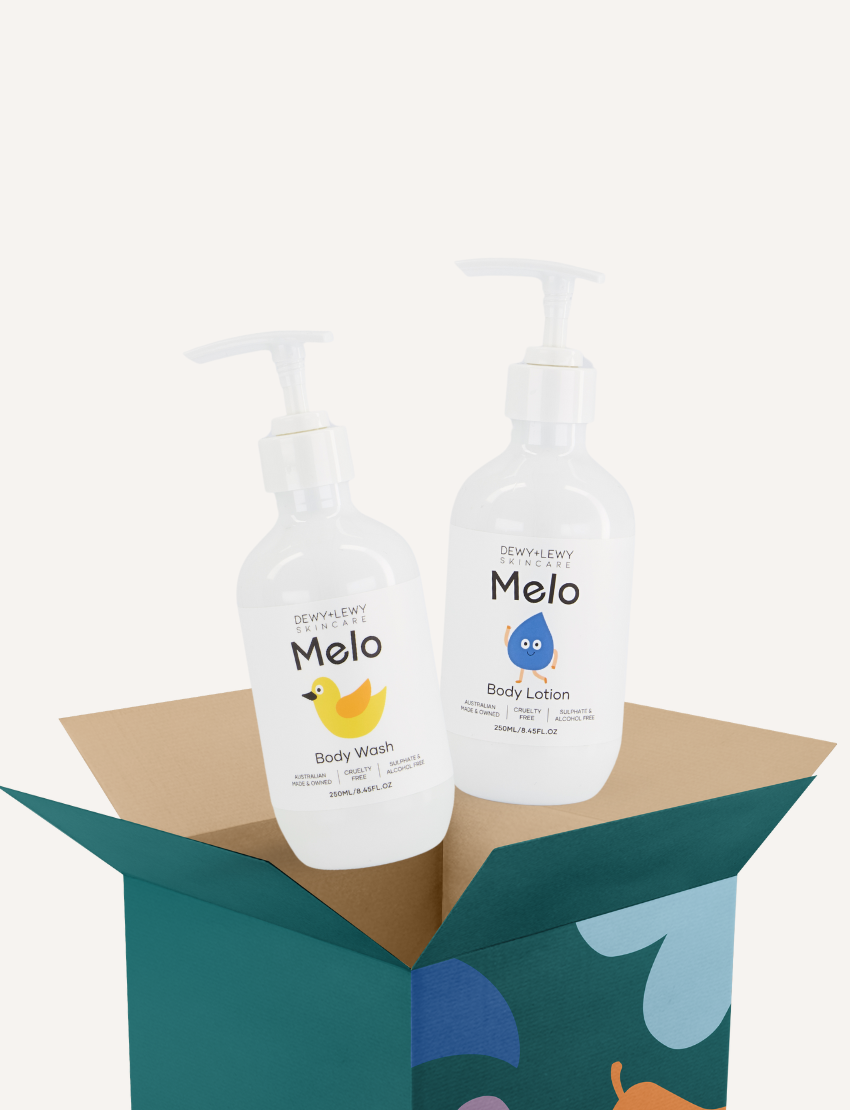 The Melo Wash Kit by Melo consists of two white pump bottles labeled "Melo Body Wash" and "Melo Body Lotion," which are elegantly arranged in an open green and brown box. The cruelty-free body wash bottle is adorned with a yellow duck graphic, while the lotion, ideal for individuals with sensory sensitivities, displays a soothing blue droplet design.