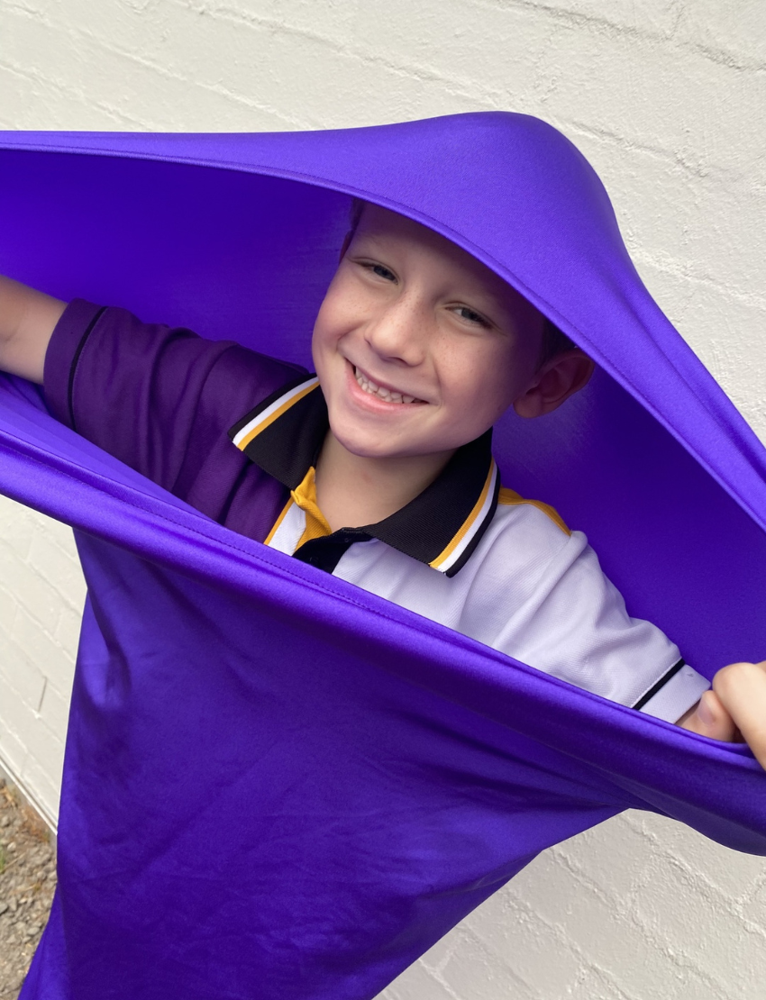 A white drawstring bag featuring the brand name "The Play Way," comes with two white cords for closing. Attached to one of the drawstrings are colorful tags with creative designs and text. Ideal for sensory regulation, this Movement Tube helps maintain emotional balance during playtime.