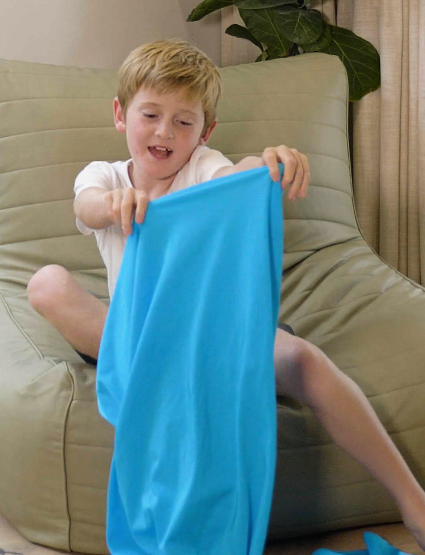 A white drawstring bag featuring the brand name "The Play Way," comes with two white cords for closing. Attached to one of the drawstrings are colorful tags with creative designs and text. Ideal for sensory regulation, this Movement Tube helps maintain emotional balance during playtime.