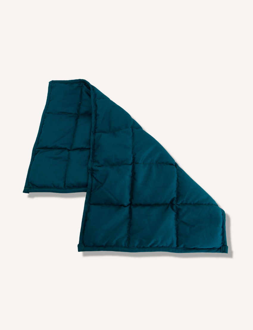 A folded, teal weighted lap pad by The Play Way is displayed on a plain white background, featuring square stitching patterns that create a grid-like appearance.