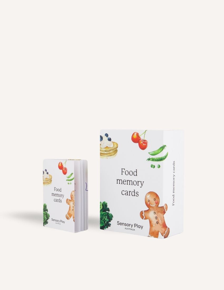 Two Sensory Play Australia "Food Memory Cards Set in Box" packages are shown. The front box displays vibrant illustrations of food items such as broccoli, a gingerbread cookie, and a pie. The back box includes instructions and game information in text and graphics, enhancing the mealtime experience through playful exploration of food.