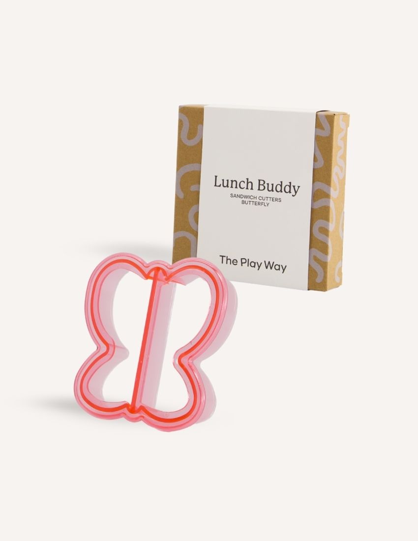 A blue dolphin-shaped sandwich cutter sits in front of a small brown and white box labeled "Lunch Buddy Sandwich Cutters Set" by The Play Way. The box, adorned with wave patterns on the sides, promises fun sandwich shapes designed to delight even the pickiest eaters.