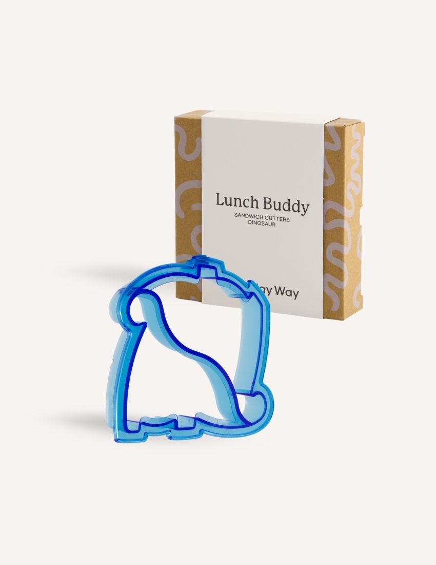 A blue dolphin-shaped sandwich cutter sits in front of a small brown and white box labeled "Lunch Buddy Sandwich Cutters Set" by The Play Way. The box, adorned with wave patterns on the sides, promises fun sandwich shapes designed to delight even the pickiest eaters.