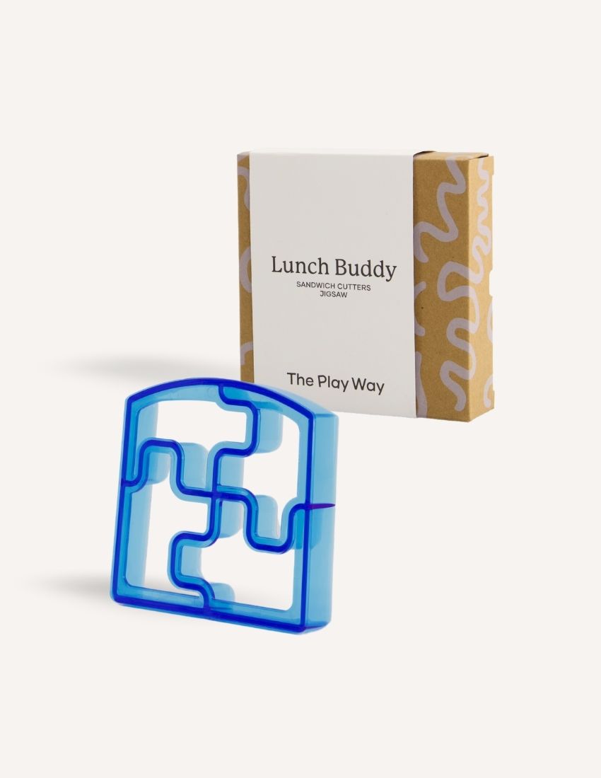 A blue dolphin-shaped sandwich cutter sits in front of a small brown and white box labeled "Lunch Buddy Sandwich Cutters Set" by The Play Way. The box, adorned with wave patterns on the sides, promises fun sandwich shapes designed to delight even the pickiest eaters.