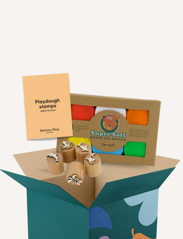 A box of the Fine Motor Practice: Playdough Kit by The Play Way, containing colorful playdough tubes and wooden stamps with various designs for creative expression, along with a booklet titled "Playdough Stamps." The box is adorned with abstract shapes and partially opened to reveal these sensory engagement tools, which are designed to enhance fine motor skills.