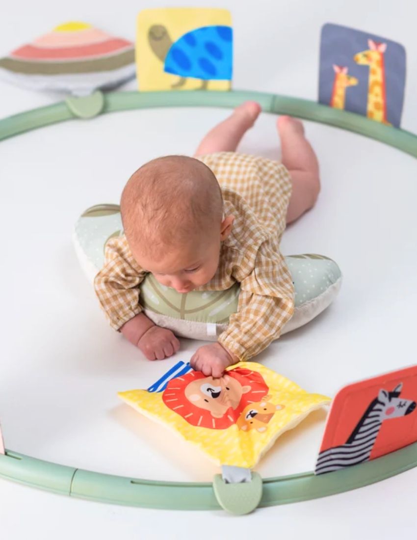 The image showcases the packaging of the "Tummy Time Trainer." The box is primarily white and purple, adorned with images of a baby using the product and featuring a baby-safe mirror. It states "Easier Development" and includes "10 Products" suitable for babies from 0 months old. The brand is TAF.