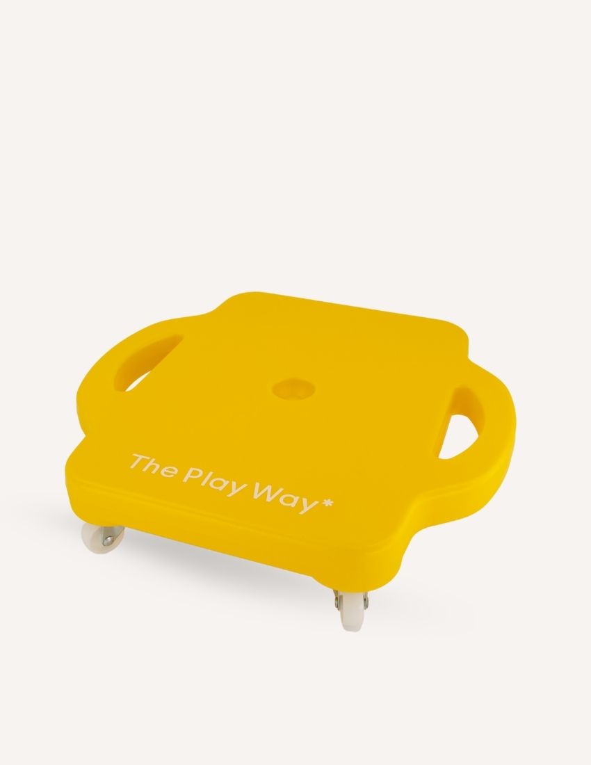 A square yellow plastic "Scooter Board" by The Play Way, featuring two built-in handles on either side and four wheels underneath. The text "The Play Way" is printed on the top surface against a plain white background.