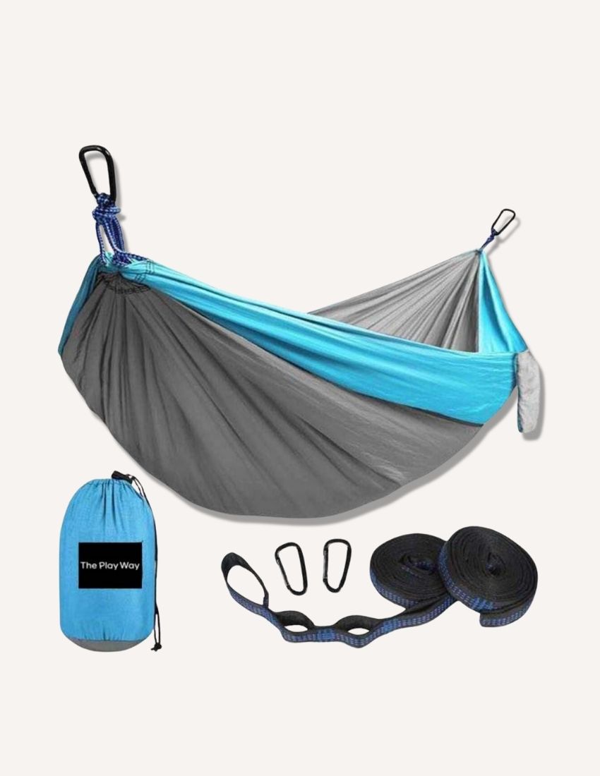 The Hammock Swing by The Play Way is shown in blue and gray, set up with black carabiners attached to straps. Below the hammock are two black straps, two additional carabiners, and a blue drawstring bag labeled "The Play Way," perfect for sensory processing and offering proprioceptive input.