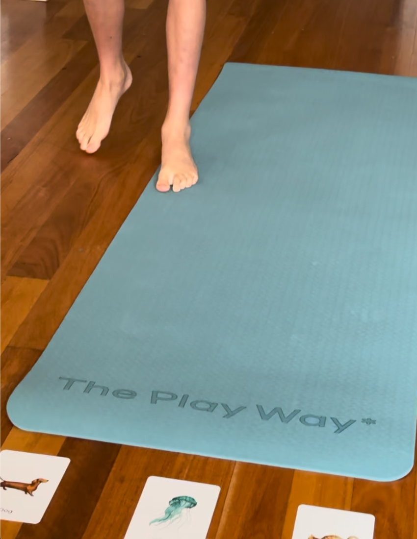 A person in a green and white striped shirt is doing a plank on a blue yoga mat from their Yoga Bundle with Large Mat by The Play Way. Positioned indoors on a wooden floor, with their head facing down and arms extended straight, the individual, practicing mindfulness, is wearing a smartwatch on their left wrist.