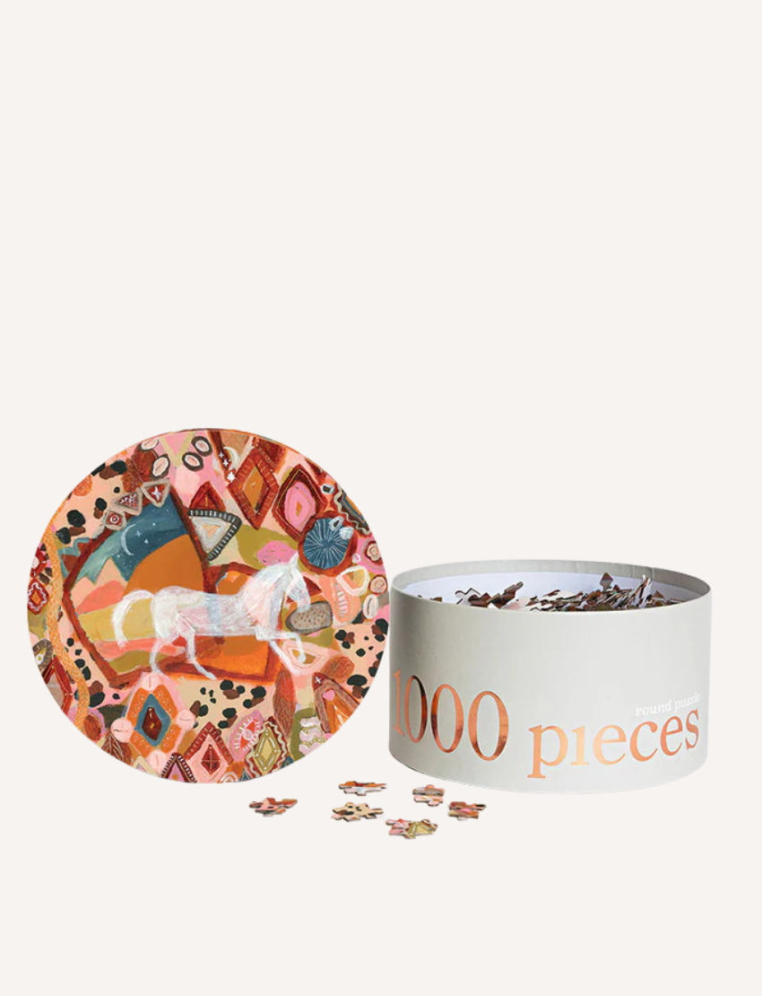 A cylindrical box labeled "1000 pieces" from Journey of Something is open, revealing scattered puzzle pieces. The box showcases a vibrant abstract design centered on a horse, suggesting the challenge of assembling this intricate 1000-Piece Round Puzzle.