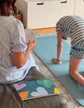 A person in a green and white striped shirt is doing a plank on a blue yoga mat from their Yoga Bundle with Large Mat by The Play Way. Positioned indoors on a wooden floor, with their head facing down and arms extended straight, the individual, practicing mindfulness, is wearing a smartwatch on their left wrist.