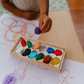 Child's hand holds a fruit crayon, a tactile activity from The Play Way Fine Motor Foundations Program for OT at home.