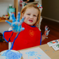 A smiling child displays a finger painting creation, a fun activity from The Play Way Fine Motor Foundations Program at home.