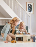 Introducing the Flexa Wooden Parking Garage: a carefully crafted wooden toy parking garage that includes a helipad and two charging stations. This structure offers parking spaces and a ramp, all set on a flat wooden base. It features primarily neutral colors with eye-catching blue and yellow accents.