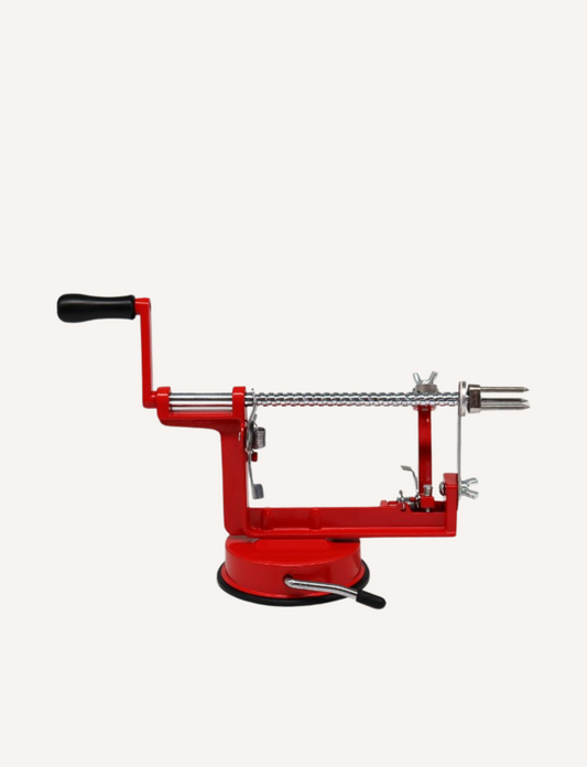 The Core Slice Peel's Apple Slinky, highlighted against a plain white background, features a red design and black handle. This device includes a stainless steel blade, manual crank, and suction base, making it ideal for efficiently peeling, coring, and slicing apples to prepare delicious fruit snacks.