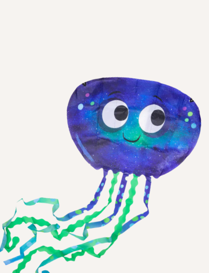 A young girl in a purple sweater and black pants holds a Jelly Kite by Tiger Tribe, designed as a blue jellyfish with big eyes and adorned with green and blue streamers. She is standing on a grassy field with trees in the background.