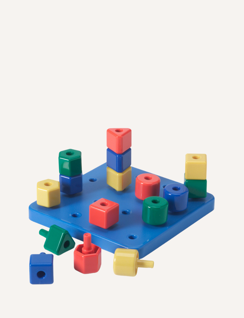 The Peggy Board by The Play Way features a blue plastic board with various geometric blocks, including red, yellow, blue, green, and orange cubes and cylinders that can be stacked on pegs. Ideal for early learning, this toy helps develop hand-eye coordination as children explore color and shape recognition. Some blocks are placed on the board while others are scattered around it.