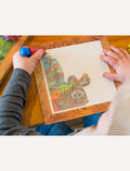 A boxed children's activity set from Tiger Tribe, named Magic Painting World - Dinosaurs, features colorful dinosaur illustrations and includes a magic paintbrush water pen. Recommended for children aged 1 and above, this portable play set boasts packaging with a charming wooden frame design.