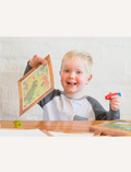 A boxed children's activity set from Tiger Tribe, named Magic Painting World - Dinosaurs, features colorful dinosaur illustrations and includes a magic paintbrush water pen. Recommended for children aged 1 and above, this portable play set boasts packaging with a charming wooden frame design.