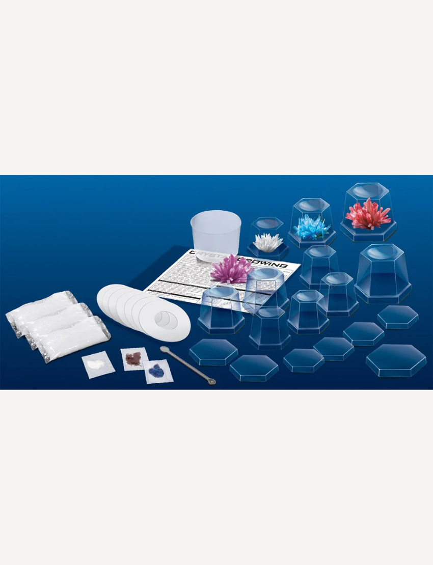 The Crystal Growing Kit (Large) by 4M Toys features an array of crystal clusters in shades of blue, red, white, purple, and pink. These vibrant crystals are beautifully presented in transparent display cases and are set against a dark surface with a matching background.