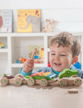 The Educational Pull-along Musical Crocodile by Ever Earth is a wooden pull-along toy train featuring colorful elements. The front section displays a frog face, followed by a segment adorned with rainbow-colored xylophone bars, and the back resembles a bear holding a bell. Connected by string and rolling on wooden wheels, this charming toy provides both fun and learning for young children.