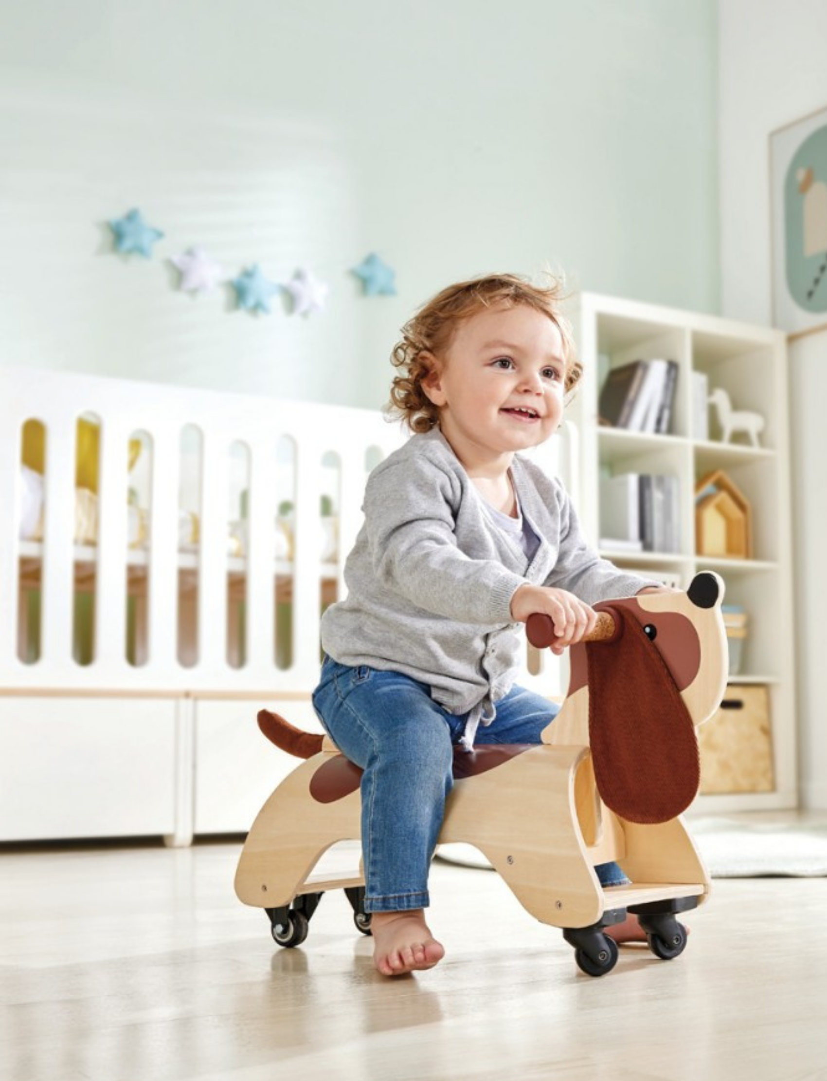 The Hape Dachshund Dog Wooden Ride On is a fun and stylish wooden toddler walker featuring four wheels, a handlebar at the dog's head, an ergonomic seat, brown felt ears, and a tail. The main body is crafted from sturdy wood with light wood shades and darker brown patches mimicking the dog's fur.