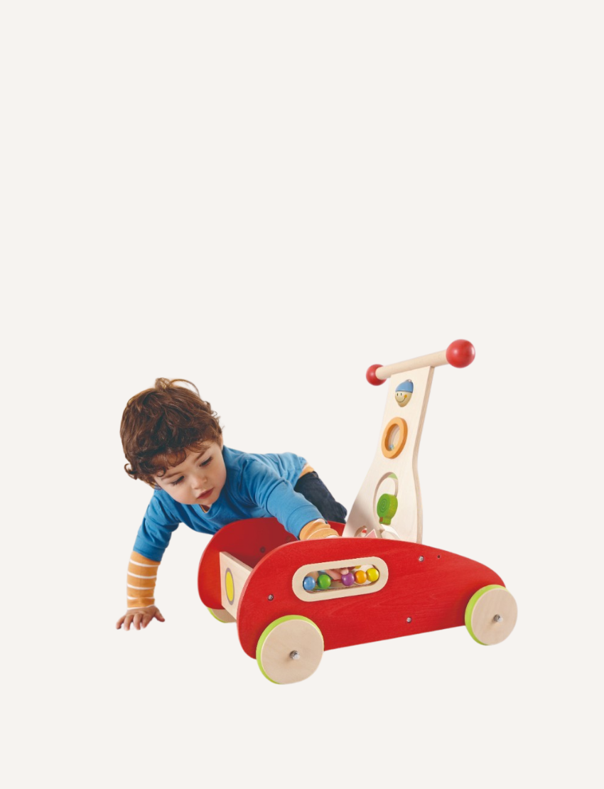 The Hape Wonder Walker is a wooden baby walker painted red with green wheels, featuring built-in toys. The walker includes a xylophone, spinning gears, and various shapes for interactive play. The handle is adorned with two red knobs, and there are small colorful details throughout.