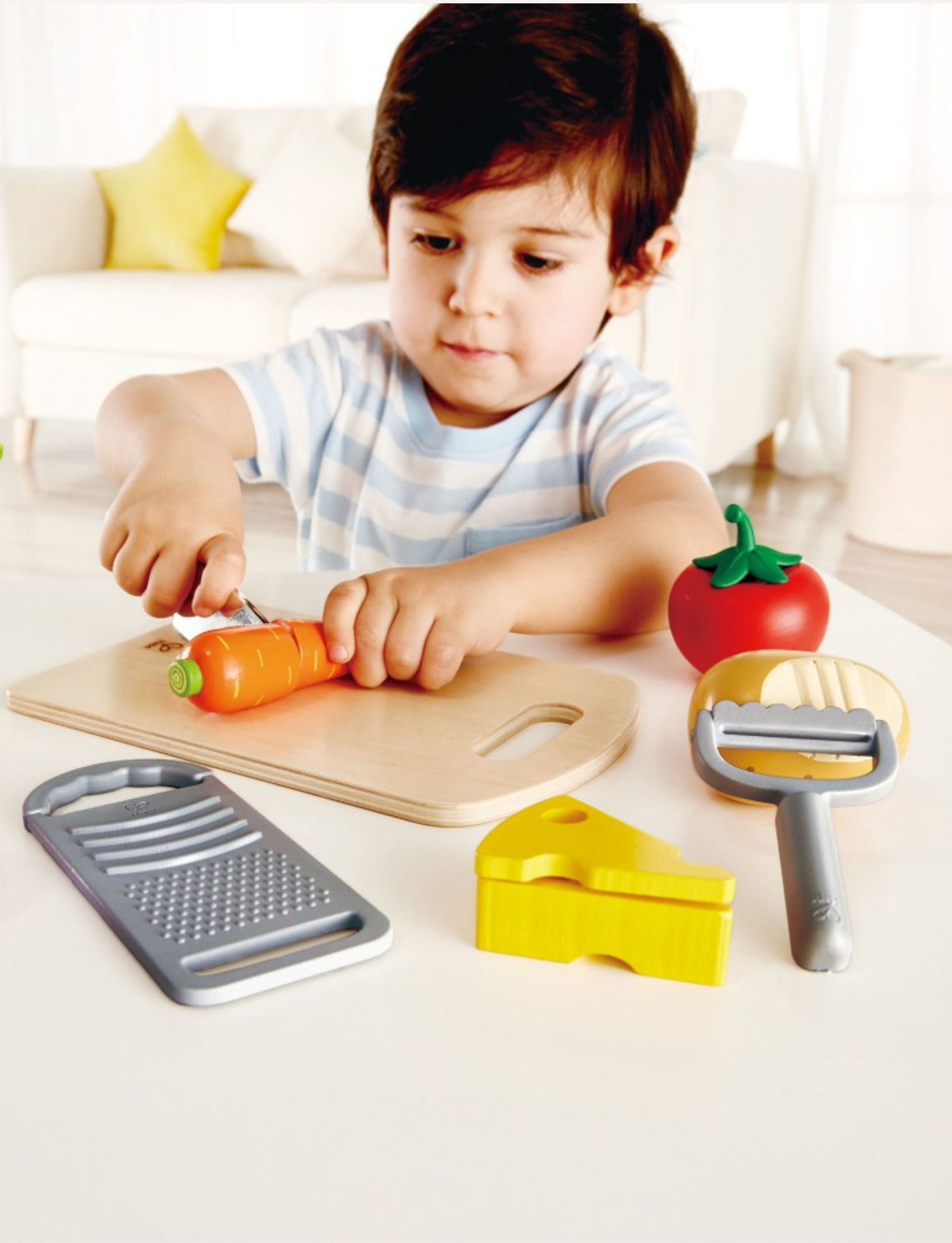 The Cooking Essentials set from Hape includes a cutting board, toy knife, cheese, and a variety of vegetables such as carrot, tomato, and radish. It also features toy onion slices, a peeler, and a grater—all perfectly arranged to spark children's culinary creativity!