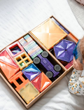 A box of the Connetix Tiles 212-Piece Magnetic Tile Mega Pack features red packaging adorned with images of vibrant geometric shapes creating a rainbow structure. The text states 