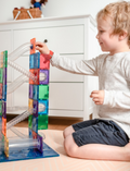 The image shows a box of Connectix 92-Piece Ball Run Pack by Connetix Tiles, ideal for STEM learning. The packaging is turquoise with geometric patterns, featuring an illustration of a colorful structure made from the tiles. The text reads 