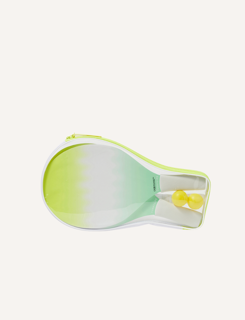 Two Sunnylife Beach Bats Sea Seeker Dip Dye with gradient green and yellow coloring and soft foam handles are placed beside two small yellow balls on a white background, making a perfect summer accessory.