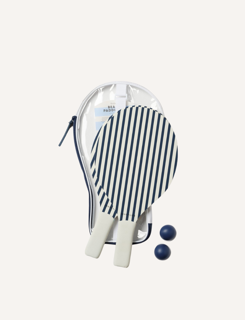 Two paddles from the Sunnylife Resort Beach Paddle Set Coastal Blue, featuring diagonal black and white stripes with white handles, are positioned opposite each other. A blue ball is next to one paddle, while another blue ball rests on one of the paddles. The background is plain white.