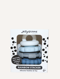 The Rainbow Stacker and Teether Toy by Jellystone Designs features a set of five silicone teething toys in assorted shapes and colors, including two circular ones with textured edges, a flat design, one shaped like a gear, and a smooth white piece. They are neatly arranged on a simple white backdrop.