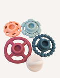 The Rainbow Stacker and Teether Toy by Jellystone Designs features a set of five silicone teething toys in assorted shapes and colors, including two circular ones with textured edges, a flat design, one shaped like a gear, and a smooth white piece. They are neatly arranged on a simple white backdrop.