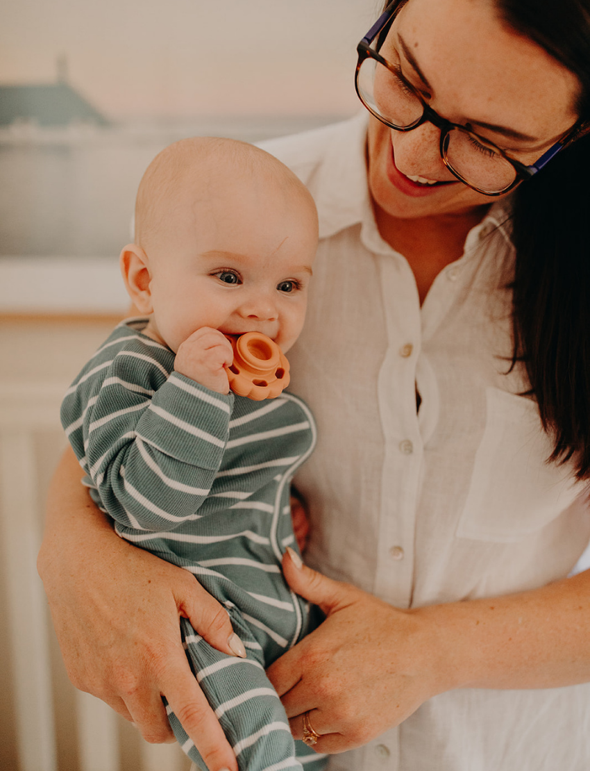 The Rainbow Stacker and Teether Toy by Jellystone Designs features a set of five silicone teething toys in assorted shapes and colors, including two circular ones with textured edges, a flat design, one shaped like a gear, and a smooth white piece. They are neatly arranged on a simple white backdrop.