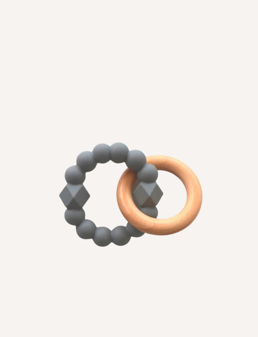 A charming Moon Teether for babies by Jellystone Designs features a beechwood teething ring connected to a second ring made up of dark gray, hexagonal, and round beads. The background is plain and light-colored.