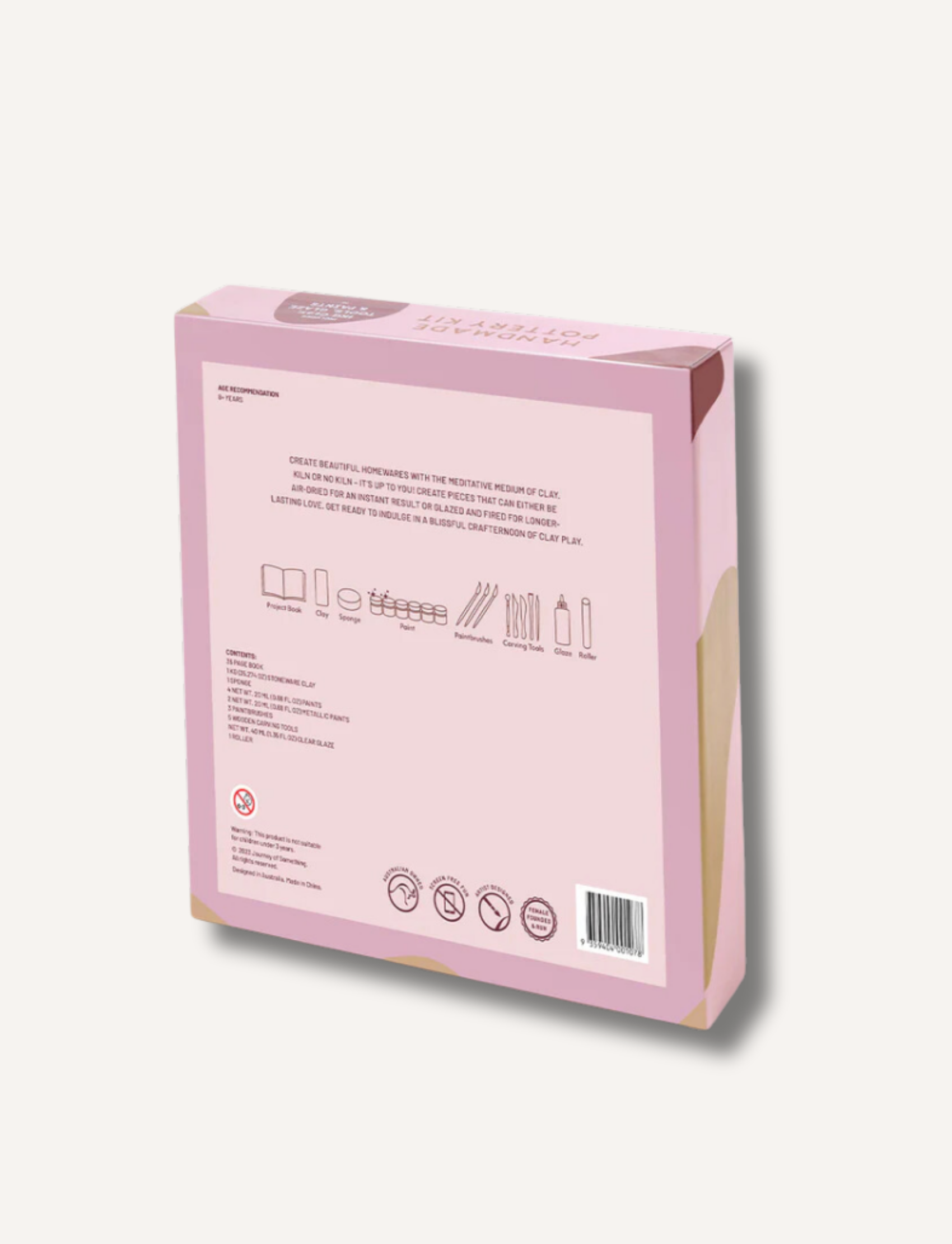 Image of a pink box containing a "Deluxe Pottery Making Kit." The box features illustrations of clay, a finished pottery piece, and tools. The top right corner indicates that the kit includes air-dry clay, tools, glaze, and paints. Perfect for personalized gifts, the brand "Journey of Something" is displayed at the top.