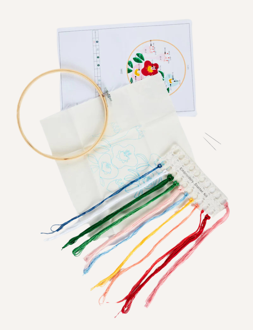 A boxed embroidery kit from Journey of Something, labeled "Embroidery Kit: Perfect for Beginners". The box, adorned in green and pink hues, features an image of a completed embroidery with vibrant flowers. This beginner-friendly craft set includes pre-printed fabric, threads, and a bamboo embroidery hoop.