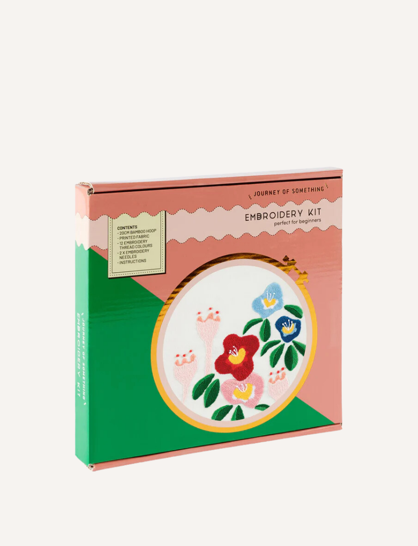 A boxed embroidery kit from Journey of Something, labeled "Embroidery Kit: Perfect for Beginners". The box, adorned in green and pink hues, features an image of a completed embroidery with vibrant flowers. This beginner-friendly craft set includes pre-printed fabric, threads, and a bamboo embroidery hoop.