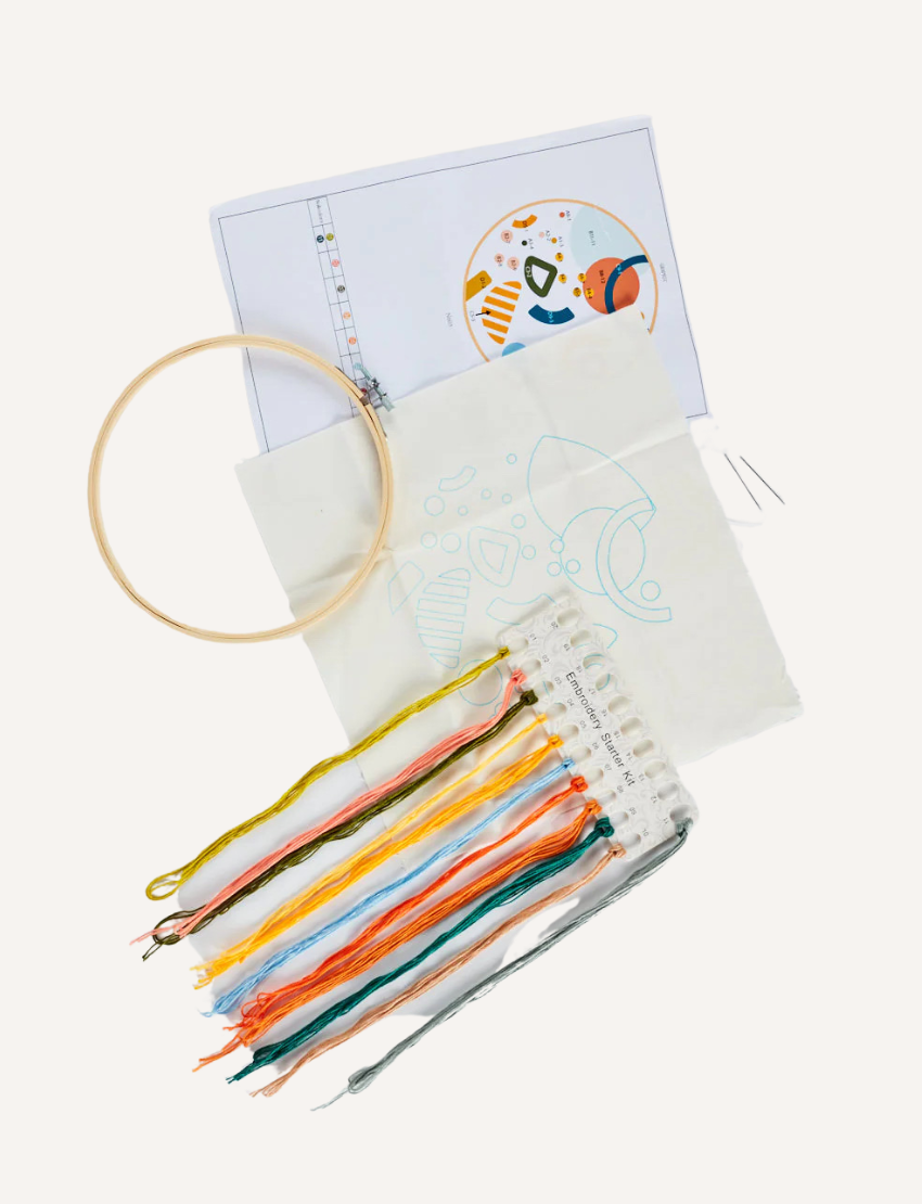 A boxed embroidery kit from Journey of Something, labeled "Embroidery Kit: Perfect for Beginners". The box, adorned in green and pink hues, features an image of a completed embroidery with vibrant flowers. This beginner-friendly craft set includes pre-printed fabric, threads, and a bamboo embroidery hoop.