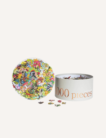 A round, colorful jigsaw puzzle with completed sections and scattered pieces is shown next to an open cylindrical container labeled "1000 Piece Puzzle" by Journey of Something. The puzzle features a vibrant design with various small images and shapes.