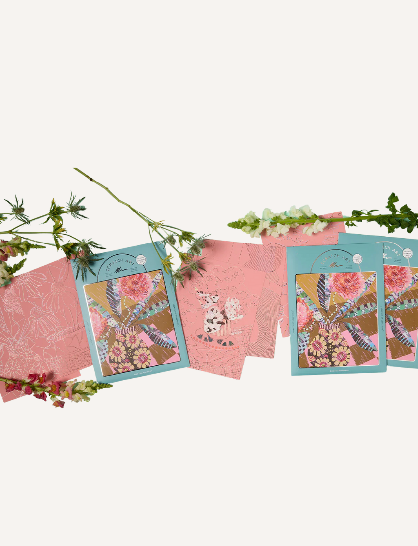 Three intricate Scratch Art greeting cards by Journey of Something, adorned with pink floral patterns, are displayed alongside two sprigs of flowers. The cards have colorful covers featuring elaborate botanical illustrations.