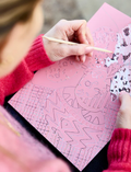 Three intricate Scratch Art greeting cards by Journey of Something, adorned with pink floral patterns, are displayed alongside two sprigs of flowers. The cards have colorful covers featuring elaborate botanical illustrations.